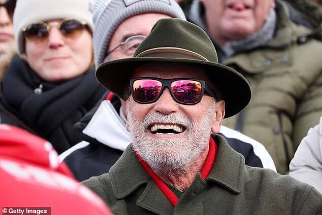 Арнольд Шварценеггер, одетый в шалфейно-зеленое пальто, красный свитер и черную альпийскую шапку с шалфейной отделкой, наблюдал за соревнованиями по мужскому слалому на чемпионате мира по горным лыжам FIS в воскресенье.