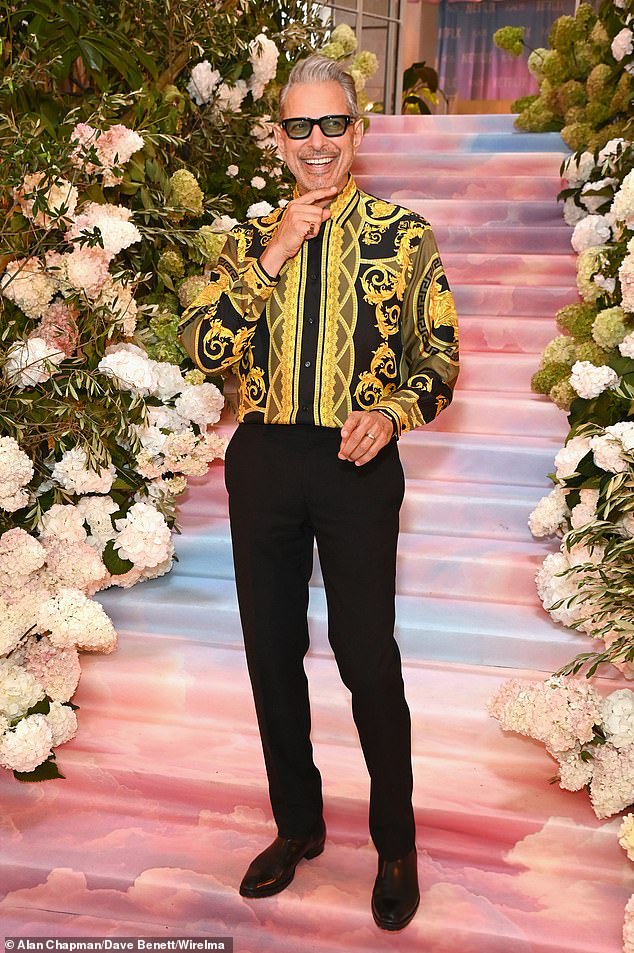 Актер выглядел странно в черно-золотой рубашке Versace, приняв участие в фотоколле черного комедийного сериала KAOS в Лондоне в среду.
